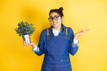 Young caucasian gardener woman holding a plant isolated on yellow background clueless and confused...