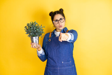 Young caucasian gardener woman holding a plant isolated on yellow background pointing with finger...