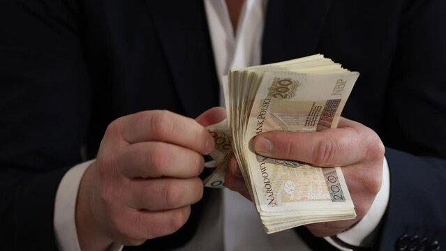 Male hands counting two hundred złoty banknotes. Only hands visible, navy blazer cuffs, white shirt.	