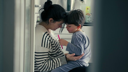 Candid mother explaining child's misbehaviour in caring warm embrace after getting hurt in tender authentic genuine loving scene at kitchen, parental guidance