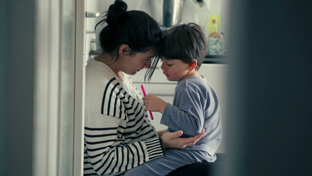 Candid mother explaining child's misbehaviour in caring warm embrace after getting hurt in tender authentic genuine loving scene at kitchen, parental guidance