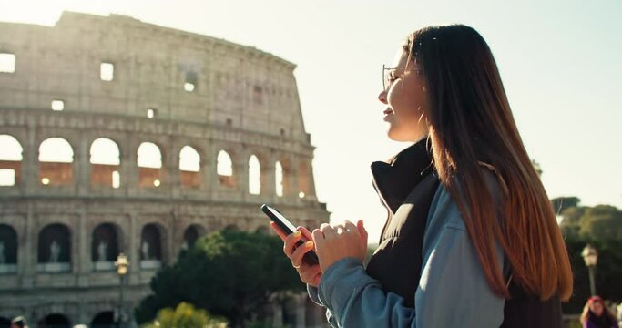 A woman looks at a map on her phone and walks near the Coliseum in Rome. A girl tourist is traveling through an old European city on the weekend. High quality 4k footage