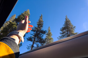Female hand reaching out the air through the open sunroof in the car