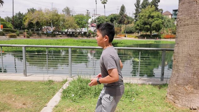 12 year old boy jogs around a park with a small lake in Los Angeles. Slow Motion.