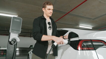 Young man travel with EV electric car to shopping center parking lot charging station in downtown...