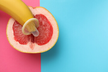 Banana with condom and half of grapefruit on color background, top view and space for text. Safe...
