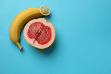 Banana with condom and half of grapefruit on light blue background, flat lay with space for text. Safe sex concept