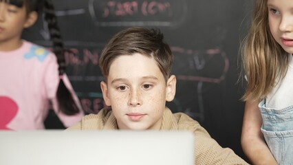 Closeup of boy using laptop programing engineering code and writing program while group of diverse...