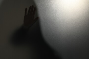 Silhouette of ghost behind glass against light grey background, closeup. Space for text