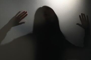 Silhouette of ghost behind glass against grey background