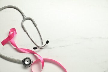 Fototapeta premium Breast cancer awareness. Pink ribbon and stethoscope on white marble table, flat lay. Space for text