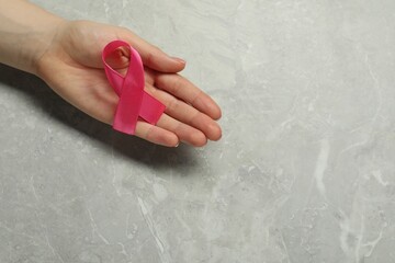Breast cancer awareness. Woman with pink ribbon at grey marble table, top view. Space for text