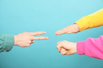 People playing rock, paper and scissors on light blue background, closeup