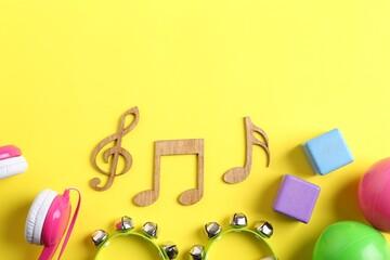 Baby song concept. Wooden notes, tambourines and toys on yellow background, flat lay. Space for text