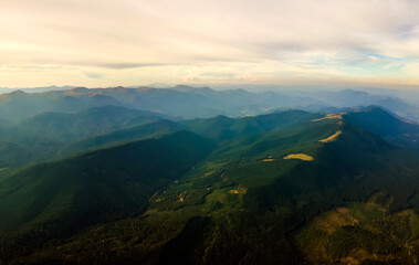 Aerial view of amazing scenery with dark mountain hills covered with forest pine trees at autumn sunrise. Beautiful wild woodland at dawn