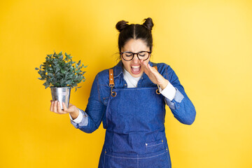 Young caucasian gardener woman holding a plant isolated on yellow background shouting and screaming...
