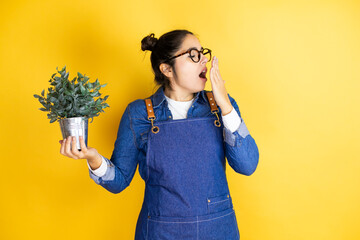 Young caucasian gardener woman holding a plant isolated on yellow background bored yawning tired...