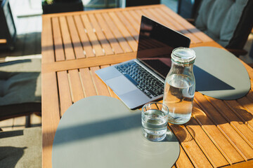 A glass of water on the background of a laptop on a summer terrace. Work in a cafe. Remote work...