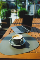 A cup of aromatic coffee on the background of a laptop on a summer terrace. Work in a cafe. Remote work online.
