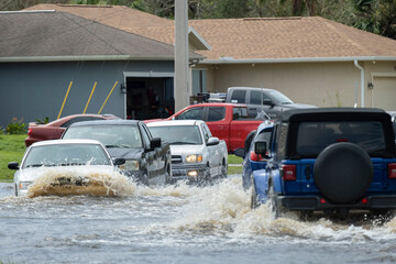 Flooded town street with moving cars submerged under water in Florida residential area after...