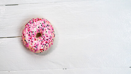 Colorful donuts on white wooden table. Sweet icing sugar food with glazed sprinkles, doughnut with frosting. Top view with copy space