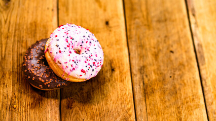 Colorful donuts on wooden table. Sweet icing sugar food with glazed sprinkles, doughnut with chocolate frosting. Top view with copy space