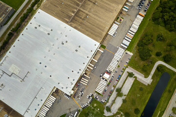 Top view of giant logistics center with many commercial trailer trucks unloading and uploading...