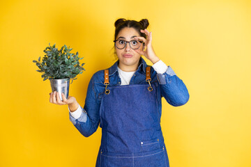 Young caucasian gardener woman holding a plant isolated on yellow background Trying to open eyes...