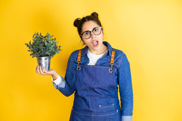 Young caucasian gardener woman holding a plant isolated on yellow background afraid and shocked...