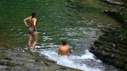 Woman and teenage boy bathing in splashing waterfall in tropical forest. Creative. Happy family enjoying fresh water from flowing waterfall in jungle.