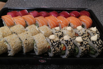 Sushi is stacked in rows and sprinkled with white and black sesame.