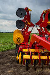 red and yellow harrow-cultivator standing folded for transportation near a field