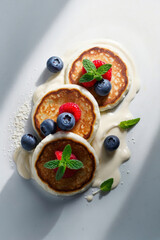 Pancakes with berries, mint leaves and delicate cream on a plate in bright daylight. 