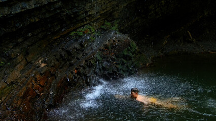 Child boy swimming in mountain pond with waterfall. Creative. Child on summertime vacation refreshing in river.