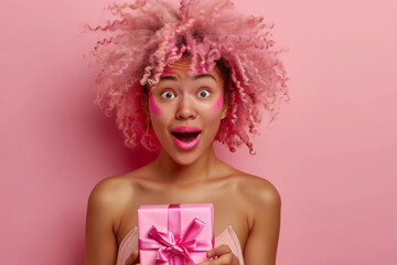 Portrait of a happy charismatic African American woman holding a gift box on a pink background. Holidays, celebrations and a feminine concept.