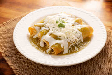 Green enchiladas. Typical Mexican dish made with a folded or rolled corn tortilla filled with shredded chicken and covered with spicy green sauce, cream, grated cheese and onion.