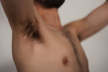 Closeup of a male underarm, as a shirtless man reaches up and reveals his thin, athletic build and...
