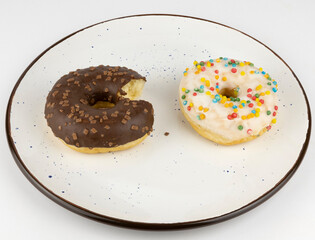 Donuts on a plate. Two chocolate donuts made of white and milk chocolate on a white plate. The...