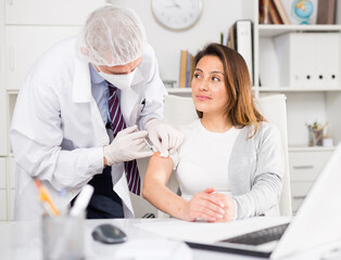 Male doctor giving vaccine to woman in company office