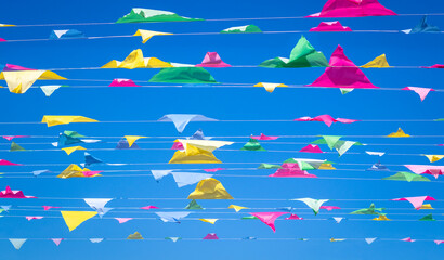 Rows of colorful bunting flags against a blue sky background. Bunting is a traditional decor, usually multi-coloured, decoration hung at parties, festivals, weddings and special events and occasions.
