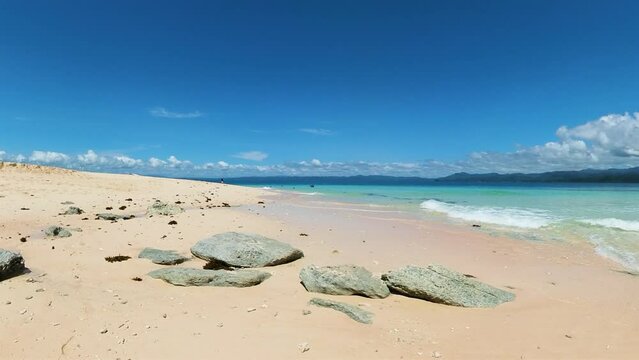Sandy beach with clear ocean waves. Blue sky and clouds. Surigao de Sur, Philippines.