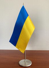 Tabletop metal flagpole with Ukrainian flag on the wooden desk.