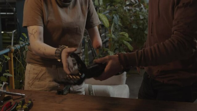 Tilt up shot of male survivor using screwdriver to fix bionic arm for girl, she putting prothesis on and thanking him for job in post apocalypse shelter