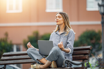 Woman meditating with laptop on urban bench - 748342418