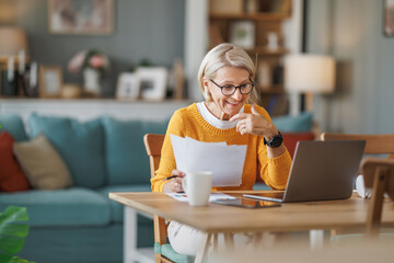 Elderly woman enjoying coffee while video conferencing - 748343204