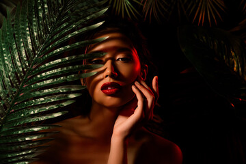 Photo of chinese japanese girl hide behind tropical palms trees touch skin on dark background