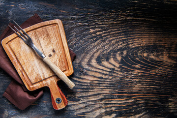 Cutting board and napkin and vintage fork on a dark wooden table. Space for text.