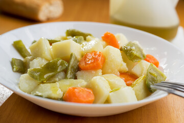Dish of cooked vegetables, potatoes, carrots, green beans and leek drizzled with extra virgin olive oil.