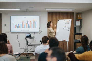 Engaged businesswoman points at whiteboard during a corporate presentation with attentive audience...