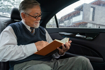 Confidence senior businessman CEO in suit wearing glasses sitting on car back seat and writing...